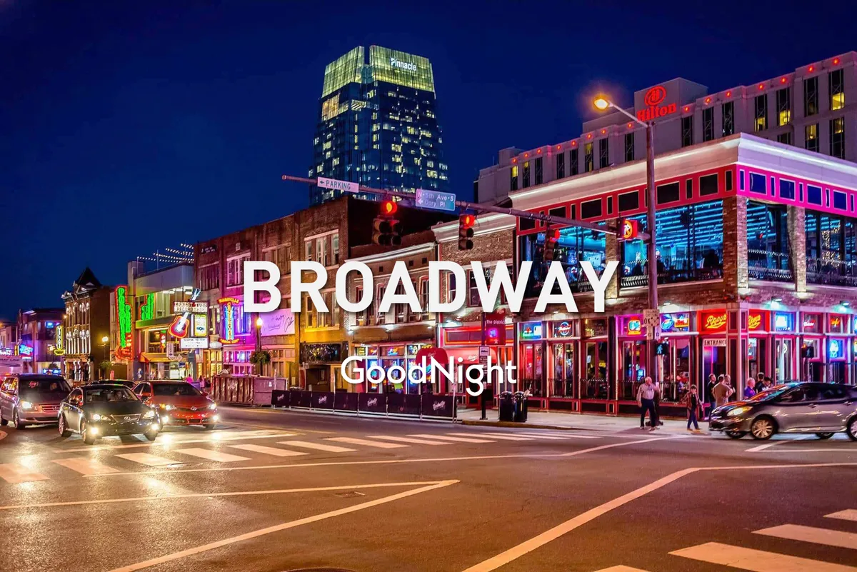 A lively street scene at night featuring neon lights, a bustling crowd, and a city skyscraper in the background. The vibrant atmosphere evokes the energy of Nashville's famous nightlife districts, with people out enjoying music, dining, and socializing.