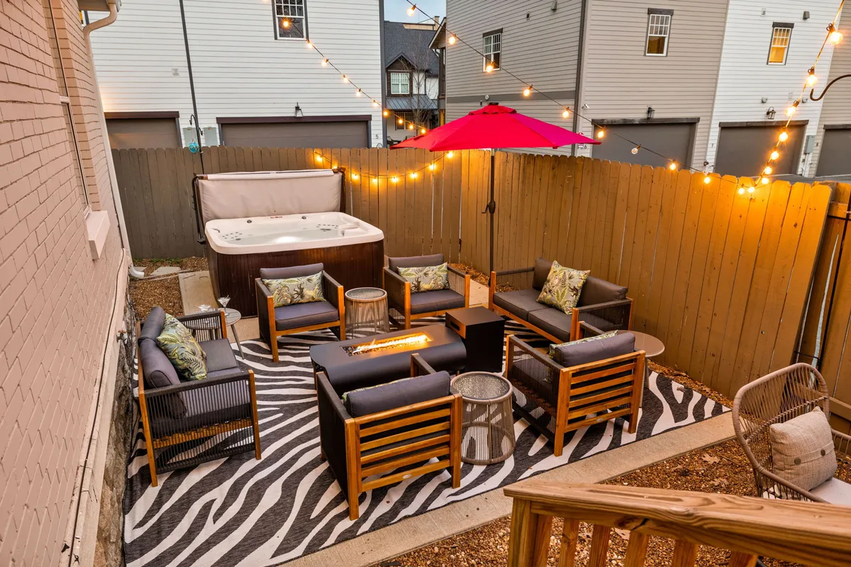 The image showcases a stylish outdoor space at a historic Nashville home, featuring a private hot tub, inviting string-lit seating, a bold zebra-striped rug, and views perfect for sunset relaxation or lively gatherings under the stars.