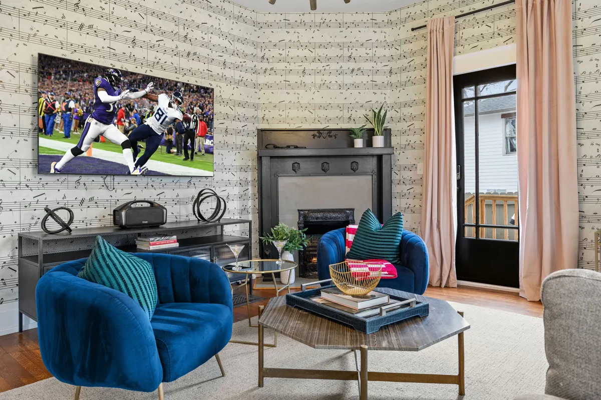 A vibrant living area with a TV showing a sports event, colorful chairs, decorative pillows, and playful musical note wallpaper. The atmosphere is cheerful and inviting, ideal for group gatherings and relaxation.
