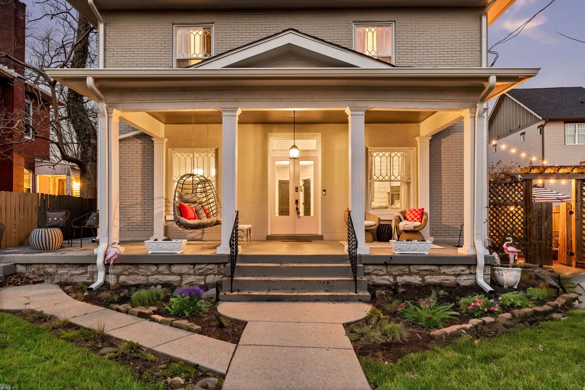 This image shows an inviting exterior porch with a hanging chair, decorative pillows, and the entrance door. The space feels cozy and welcoming, suggesting a relaxing spot to enjoy a drink or conversation while taking in the neighborhood's atmosphere.