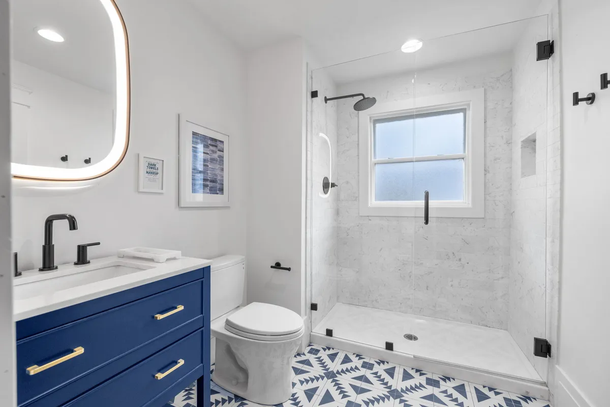 A fresh and inviting bathroom with blue cabinetry, a glass-enclosed shower, and decorative tiles. The layout offers both functionality and style, enhancing the sense of personal retreat within the home.