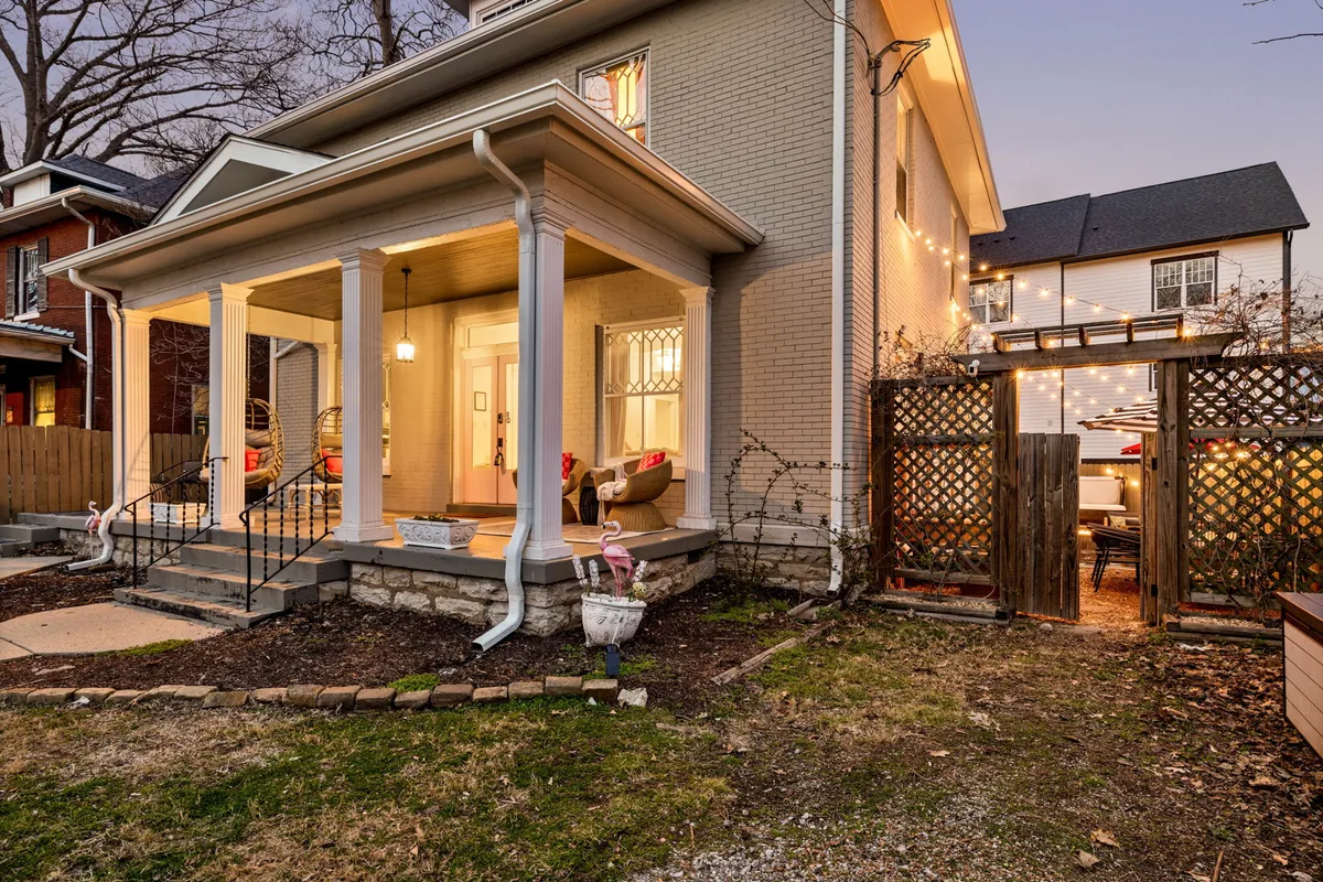 A view of a welcoming front porch with decorative columns, outdoor lighting, a garden area, and an outdoor dining space. The ambiance suggests relaxed gatherings, evening conversations, and a retreat from the city bustle.