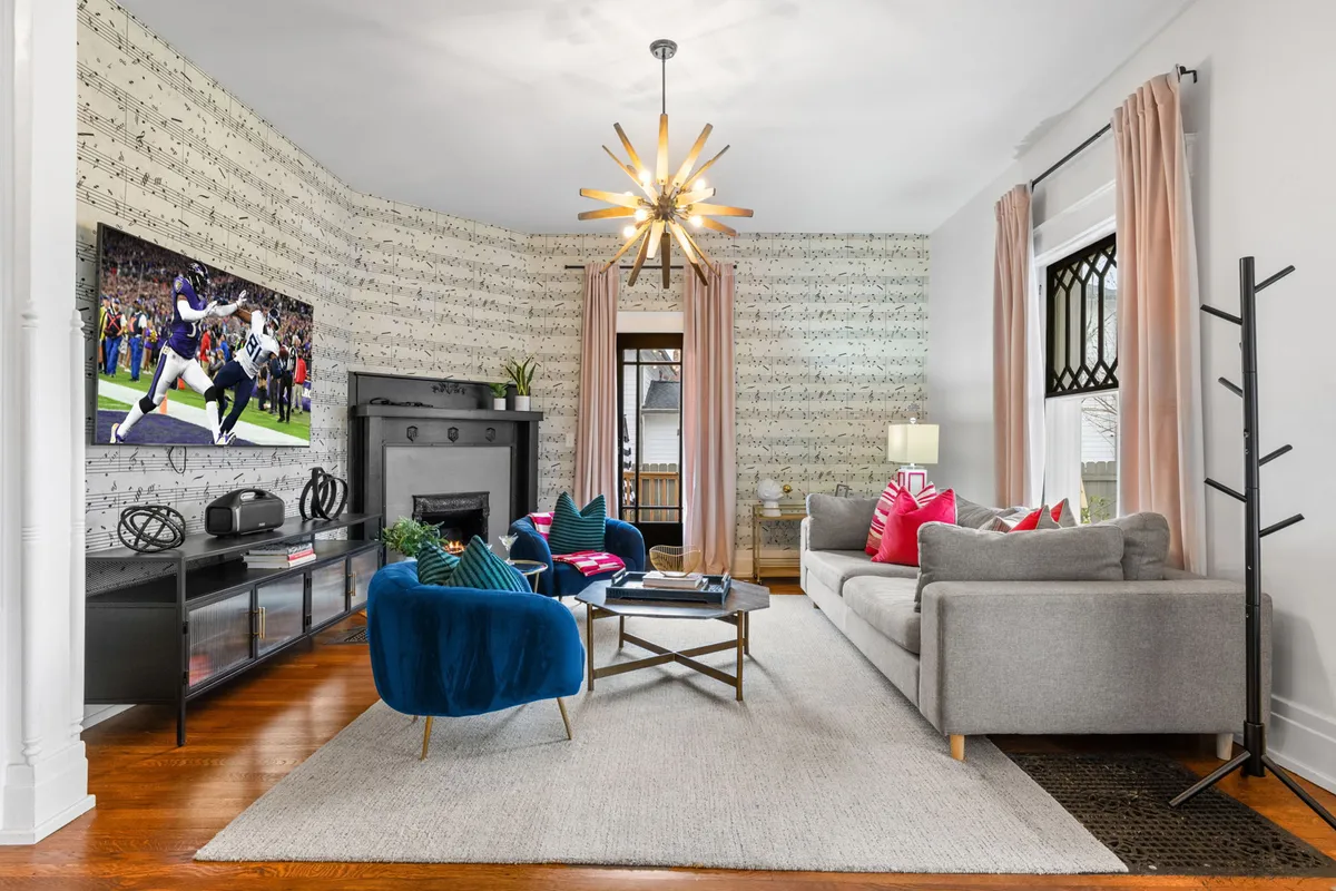 A playful and modern living room with a large TV displaying a sports scene, colorful couch cushions, a modern chandelier, and striking musical note wallpaper. The space is both stylish and comfortable, echoing Music City's spirit.