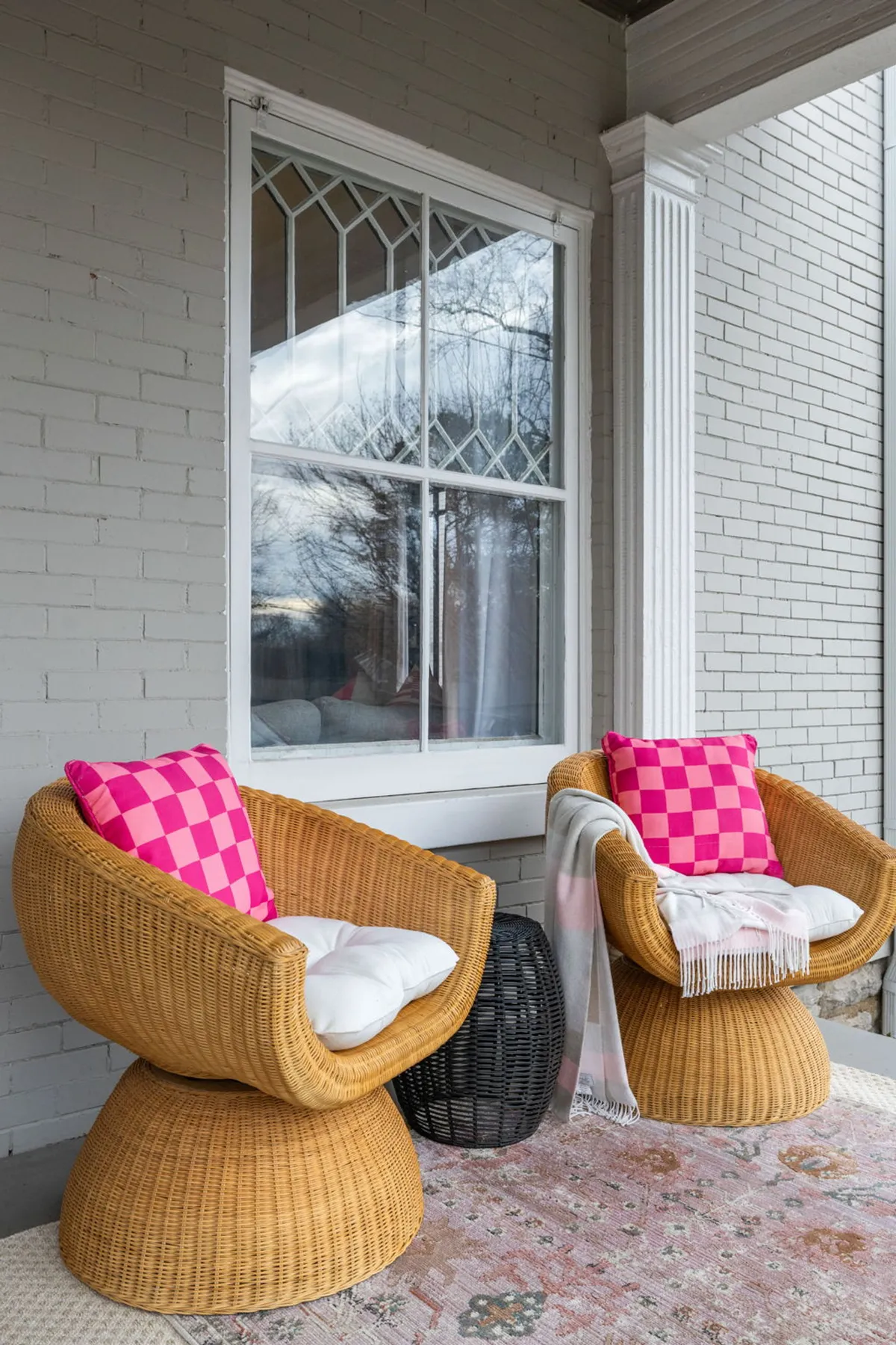 A cozy outdoor seating area featuring two wicker chairs with colorful pillows, a textured rug, and a decorative blanket, evoking a relaxed and welcoming environment for informal gatherings or after-work unwinding.