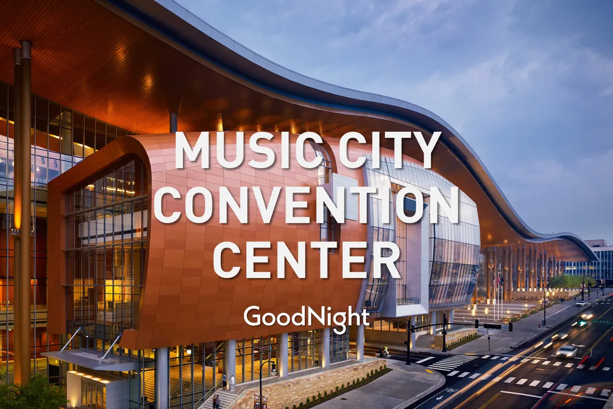 A striking exterior shot of the Music City Center, highlighting its curved glass facade illuminated by warm lighting, capturing the energy of a major conference destination just minutes away.