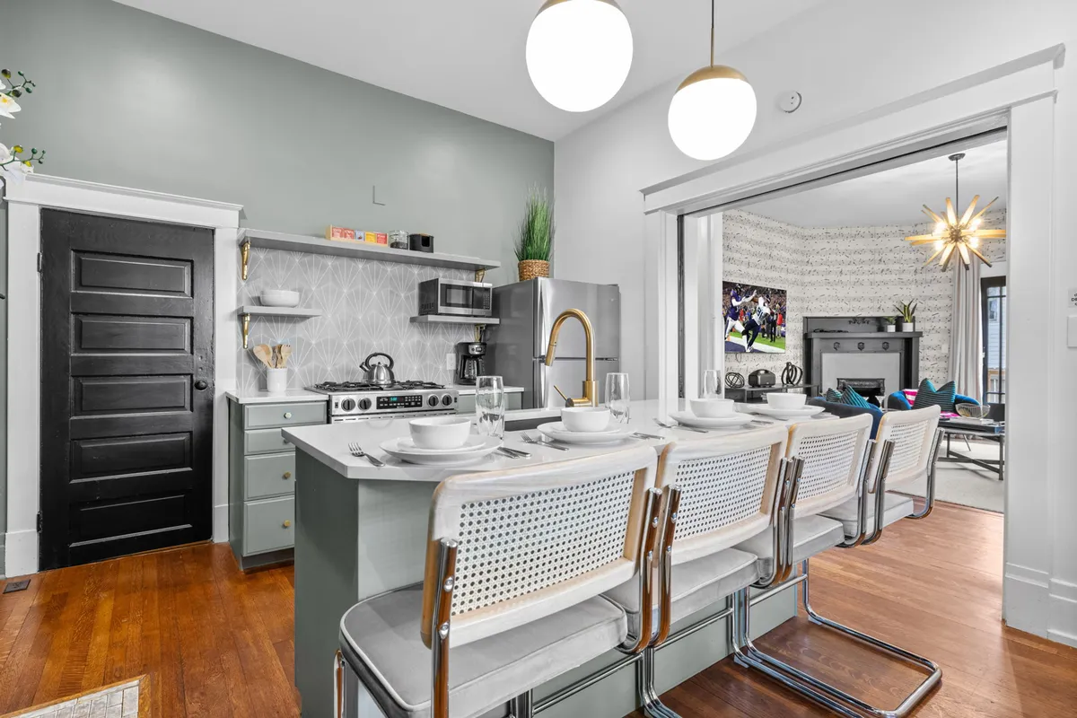 A bright, open kitchen with a central island, seating, decorative lighting, and wall decor. The space feels ideal for cooking, entertaining, or gathering over a meal, with a clear flow from living areas.